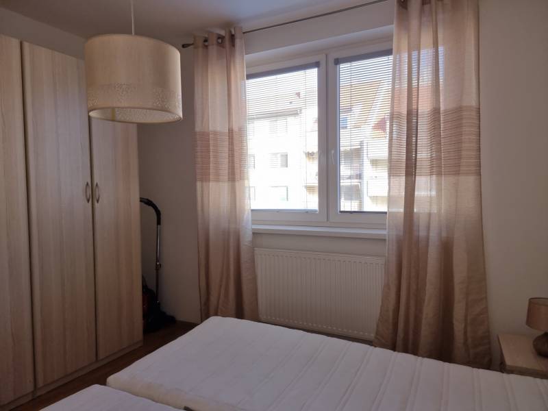 Schlafzimmer in einer 2-Zimmer-Wohnung mit Bett, Schrank und Fenster mit beigefarbenen Vorhängen.