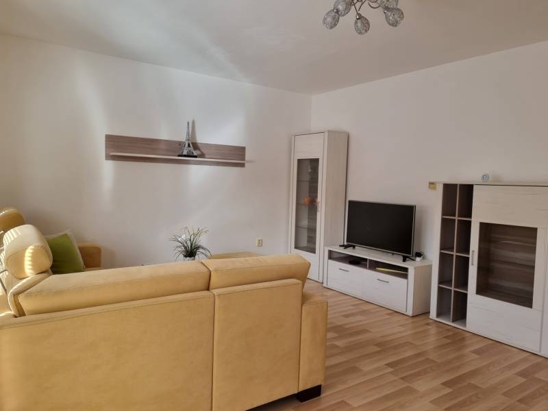 Wohnzimmer in einer 2-Zimmer-Wohnung mit beigem Sofa und Fernseher auf einem weißen Schrank.