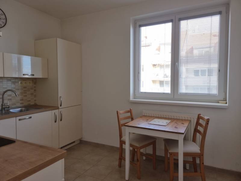 Küche in einer 2-Zimmer-Wohnung mit einem einfachen Tisch für zwei Personen und einem Fenster mit Rollläden.