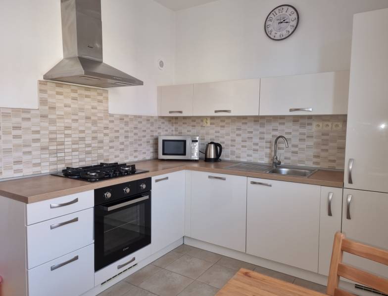 Küche mit weißen Schränken, Dunstabzugshaube und Geräten in einer 2-Zimmer-Wohnung.