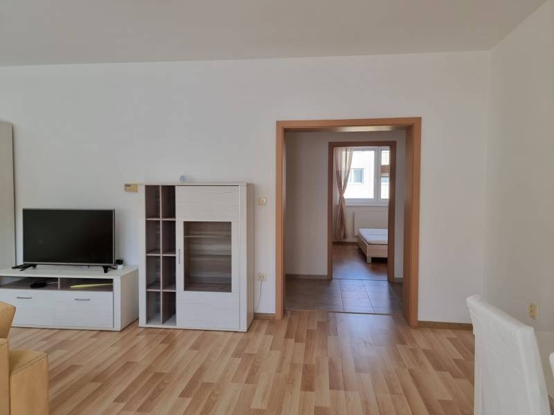 Wohnzimmer mit Fernseher, weißen Möbeln und Blick ins Schlafzimmer, 2-Zimmer-Wohnung.