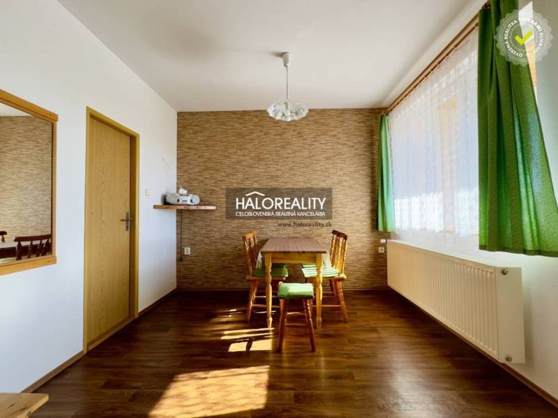 Essbereich in einem Einfamilienhaus mit Tisch und Stühlen, Holzboden, grüne Vorhänge.