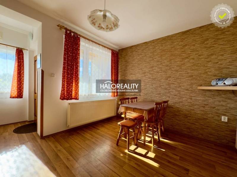 Innenraum eines Einfamilienhauses mit Holztisch und Stühlen am Fenster mit roten Vorhängen.