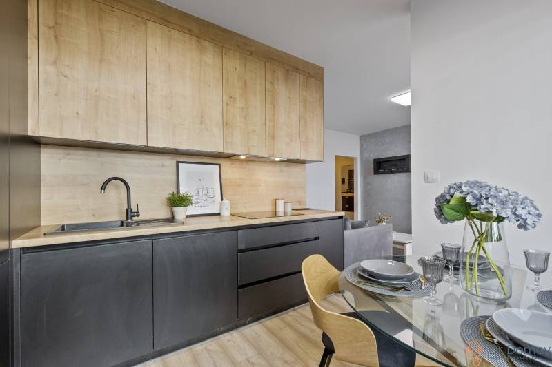 Küche in einer 2-Zimmer-Wohnung mit Holzschränken, Esstisch mit Blumen.