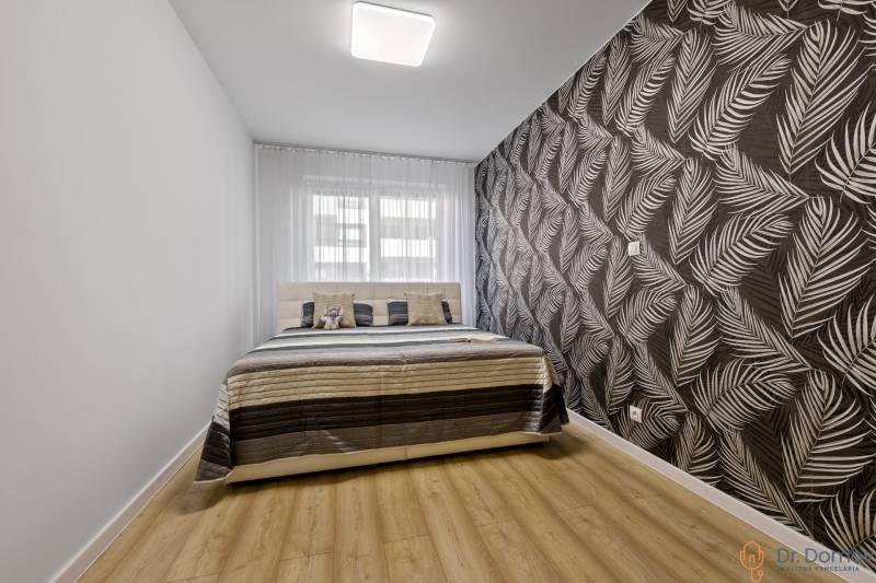 Schlafzimmer mit Bett und gemusterten Tapeten in einer 2-Zimmer-Wohnung.
