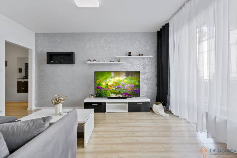 Wohnzimmer in einer 2-Zimmer-Wohnung mit Fernseher, grauer Wand und Holzboden.