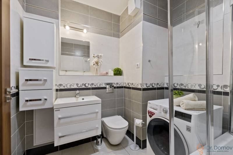 Badezimmer in einer 2-Zimmer-Wohnung mit Dusche, Waschmaschine und Waschbecken mit Spiegel.