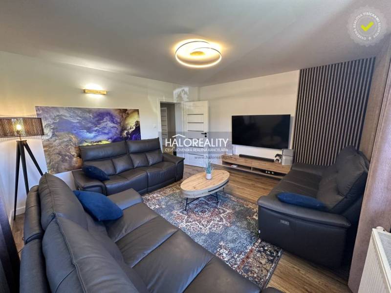 Wohnzimmer in einem Einfamilienhaus mit schwarzen Sofas, Fernseher und abstraktem Bild an der Wand.