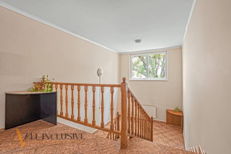 Innenraum eines Büros mit Treppe, Geländer, Fenster und Pflanze auf einem Eckschrank.