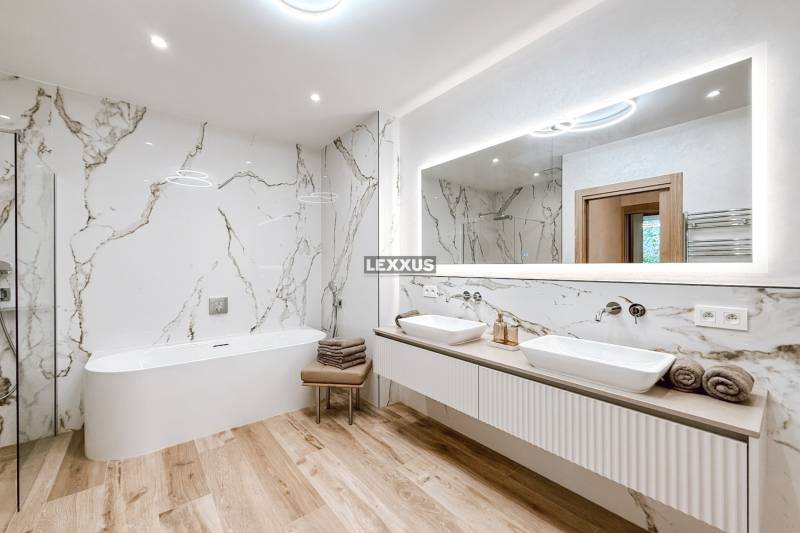 Badezimmer mit Badewanne und Doppelwaschbecken in einer 4-Zimmer-Wohnung, Marmorwände und Holzboden.