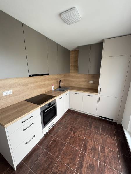 Küche in einer 2-Zimmer-Wohnung mit Holzschränken und dunklen Fliesen.