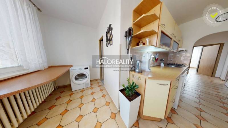 Küche in einer 3-Zimmer-Wohnung mit Waschmaschine, Küchenzeile und einer Pflanze auf dem Boden.