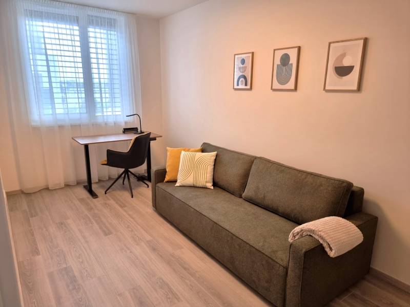 Ein Zimmer in einer 3-Zimmer-Wohnung mit einem Sofa, einem Tisch, einem Stuhl und modernen Bildern an der Wand.
