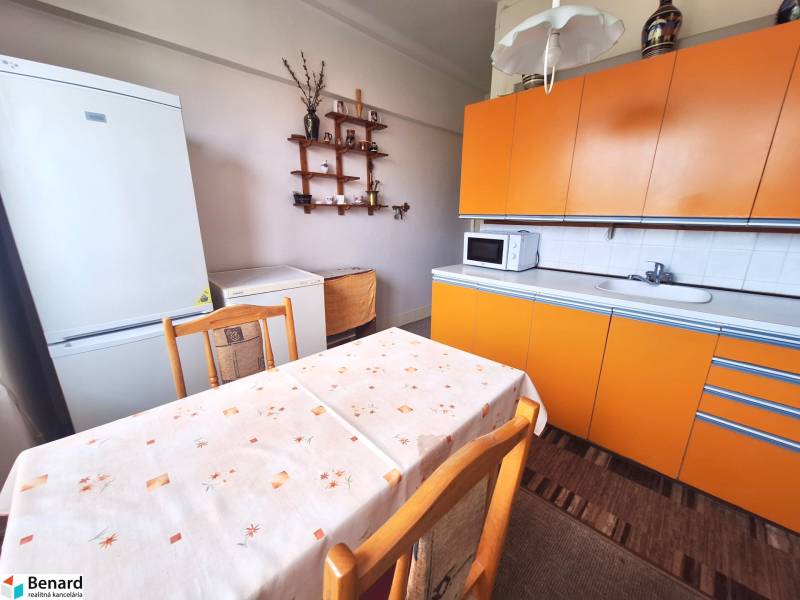 Küche in einer 2-Zimmer-Wohnung mit orangefarbener Küchenzeile, weißem Kühlschrank und Esstisch.