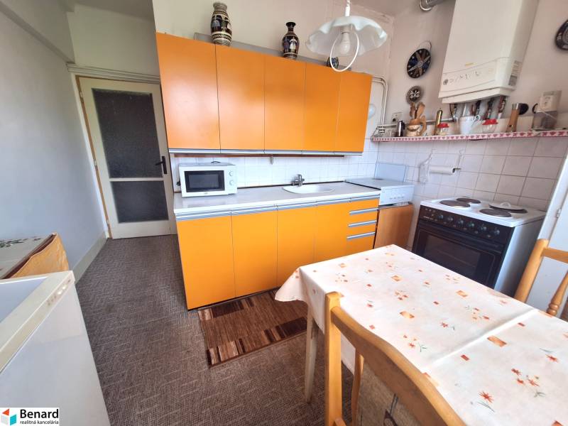 Eine Küche mit einer orangefarbenen Küchenzeile und einem Esstisch in einer Zweizimmerwohnung.