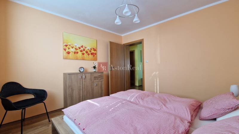Schlafzimmer in einer Ferienwohnung mit Bett, Kleiderschrank, Sessel und Blumenbild.