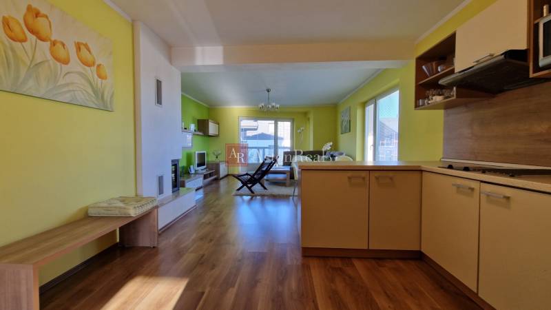 Innenraum einer Ferienwohnung mit Holzboden, Sessel und Küchenzeile in warmen Farben.