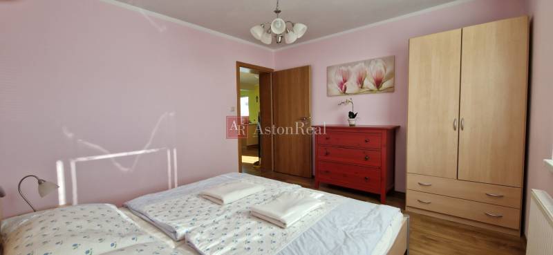 Schlafzimmer im Ferienapartment mit Schrank, roter Kommode und Blumenbild.