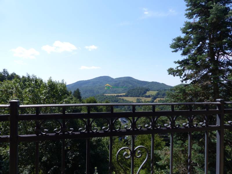 Blick von der Hütte auf das Gebirge in Štiavnické Bane, eingerahmt von einem Metallgeländer und Bäumen.