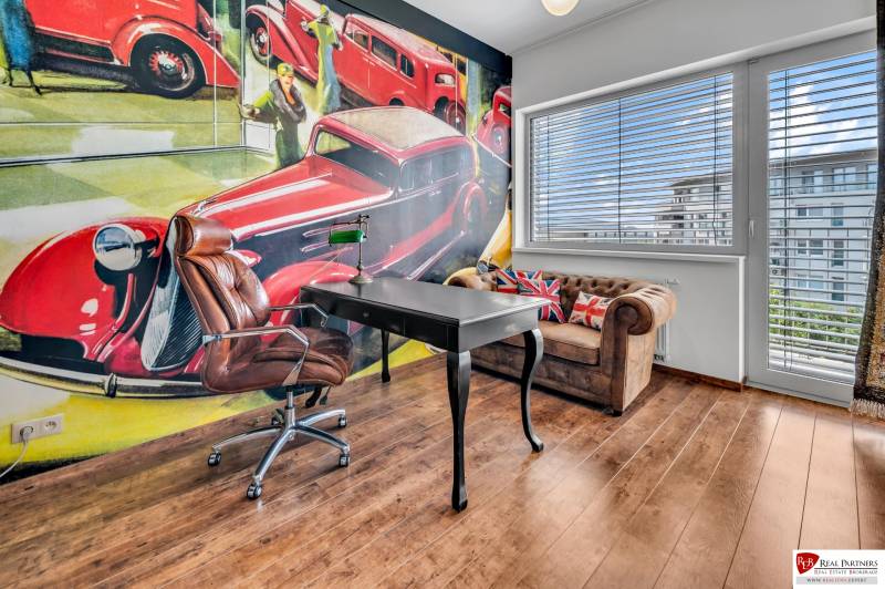 Ein Büro mit einem Ledersessel, einem Tisch und einem künstlerischen Wandgemälde in einer Vierzimmerwohnung.