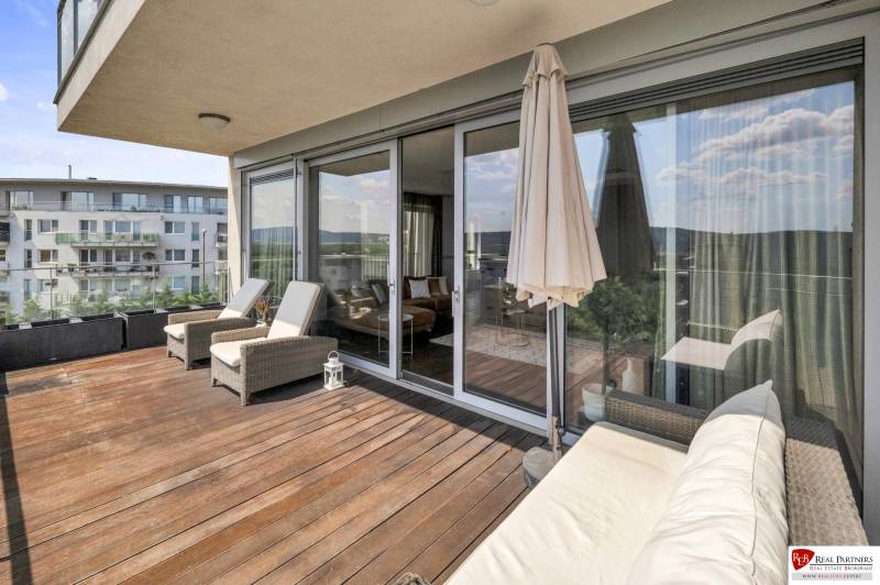 Die Terrasse einer 4-Zimmer-Wohnung in Bratislava - Karlova Ves mit bequemen Liegestühlen und einem Sofa.