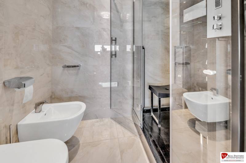 Badezimmer in einer 4-Zimmer-Wohnung mit Duschkabine, Bidet und glänzenden Fliesen.