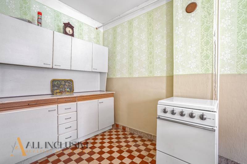 Eine Küche mit weißen Schränken, einem Herd und gemusterten grünen Tapeten in einem Einfamilienhaus.