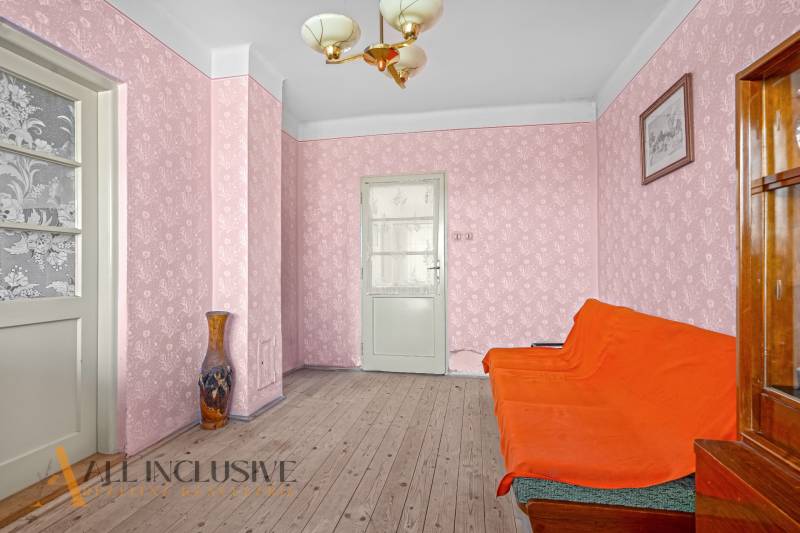 Ein Zimmer in einem Einfamilienhaus mit einem orangefarbenen Sofa, rosa Tapete und einer Vase auf dem Holzboden.