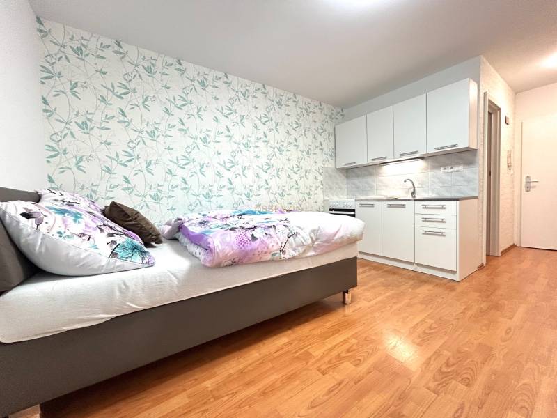 Einzimmerwohnung mit Bett, Küchenzeile und Blumenmuster an der Wand.