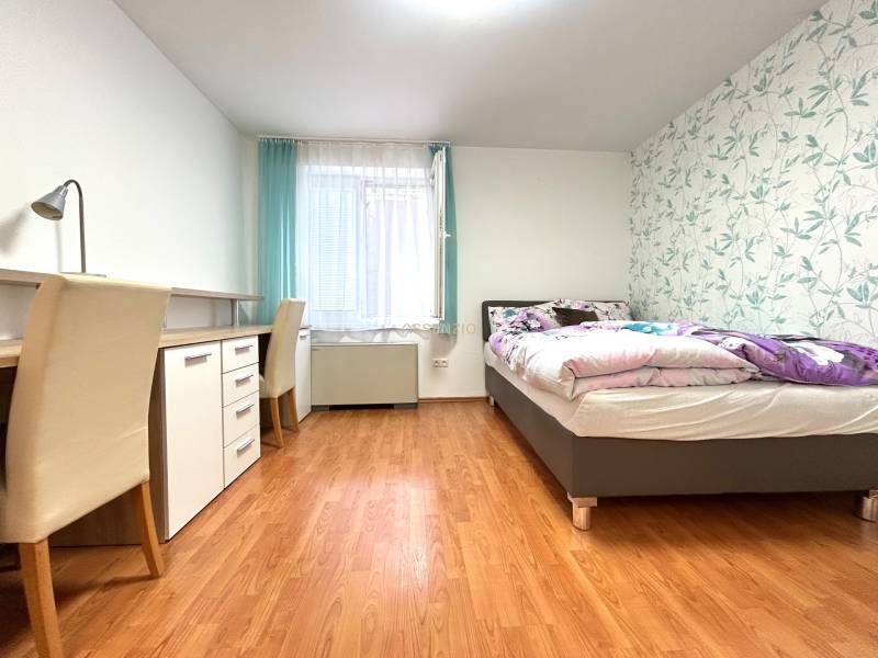Schlafzimmer in einem Einzimmerapartment mit Arbeitstisch, Bett und dekorativer Tapete.
