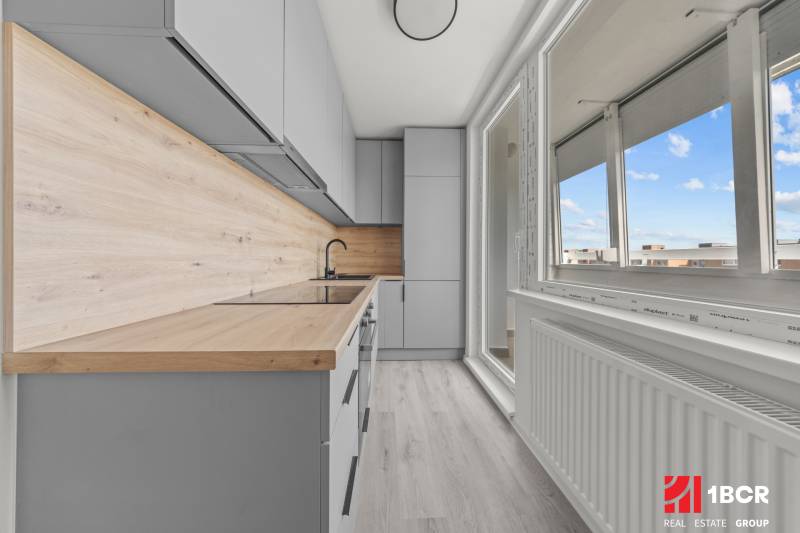 Küche in einer 2-Zimmer-Wohnung mit heller Holzverkleidung und großem Fenster.
