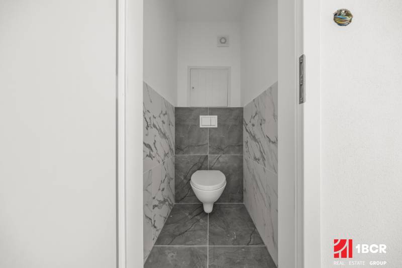 Badezimmer mit Toilette und Marmorfliessen in einer 2-Zimmer-Wohnung.
