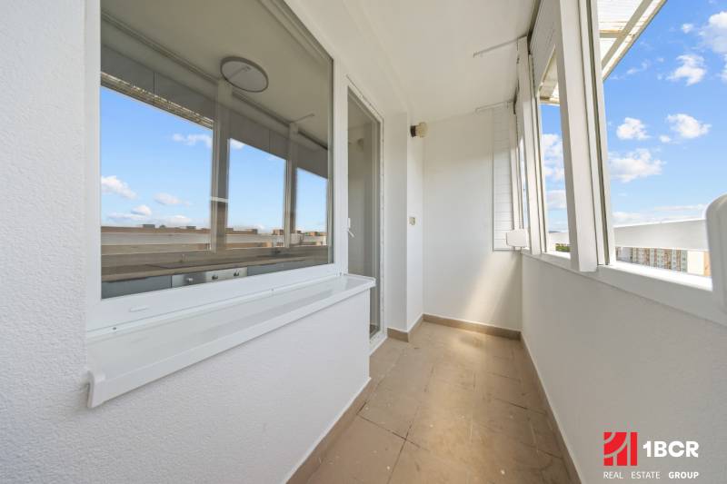 Ein heller Balkon einer 2-Zimmer-Wohnung mit Blick auf die umliegenden Dächer und den blauen Himmel.