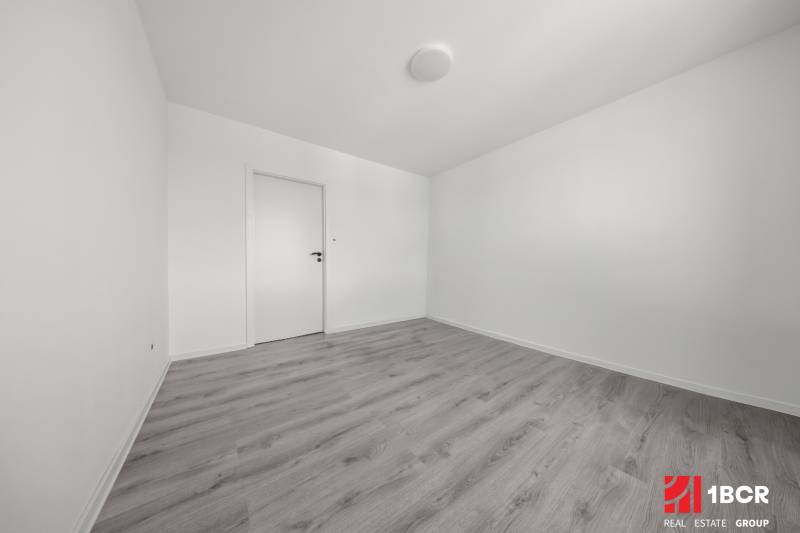 Ein leerer Raum mit weißen Wänden und grauem Boden in einer Zweizimmerwohnung.