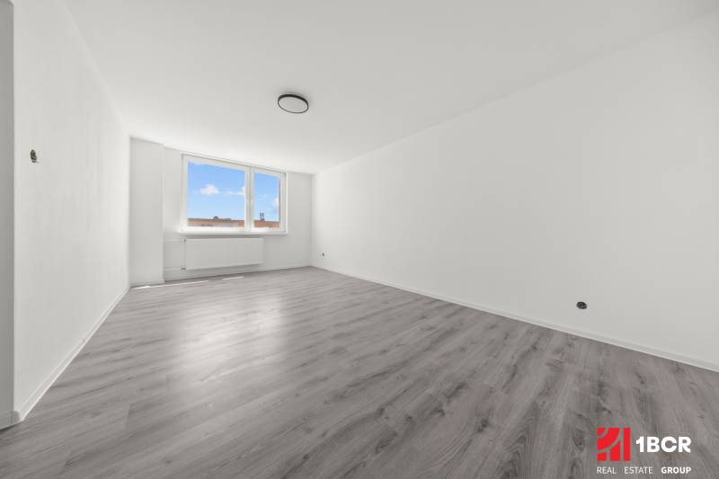 Geräumiges Zimmer mit Holzboden und großem Fenster in einer 2-Zimmer-Wohnung.