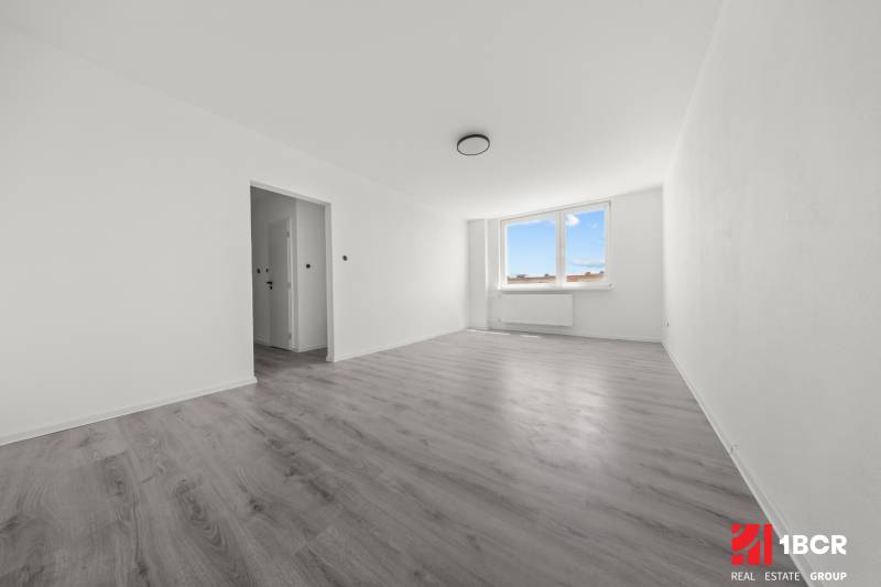 Ein geräumiges Zimmer mit einem großen Fenster und hellem Boden in einer 2-Zimmer-Wohnung.