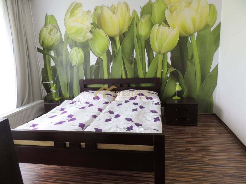 Schlafzimmer in einer 2-Zimmer-Wohnung mit Tapete mit Tulpen und einem Doppelbett mit Holzrahmen.