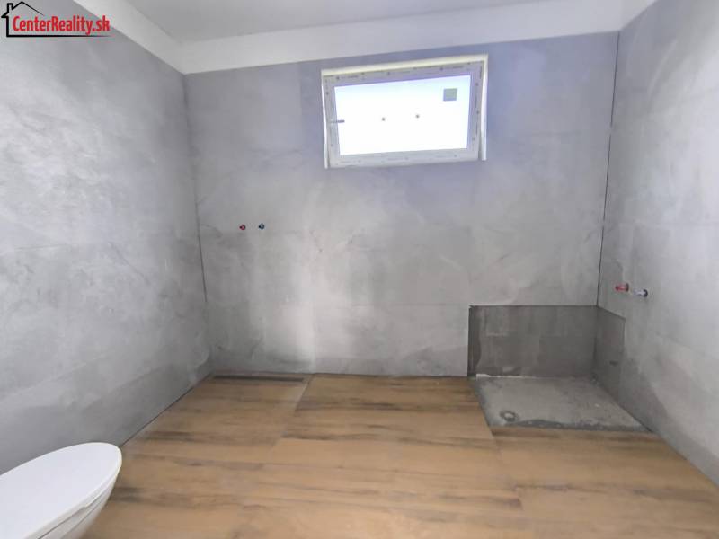 Ein Badezimmer in einem Einfamilienhaus mit Fliesen, bereit zur Installation, Licht durch ein kleines Fenster.