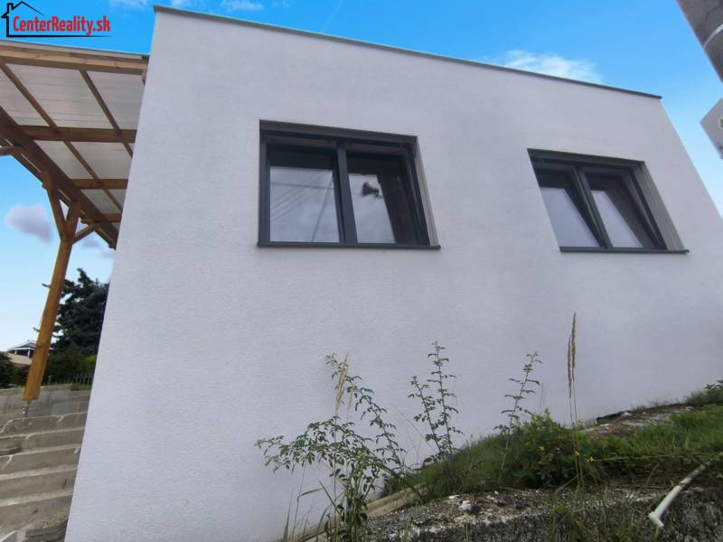 Ein Einfamilienhaus in Malé Kršteňany mit zwei großen Fenstern und einem hölzernen Unterstand.