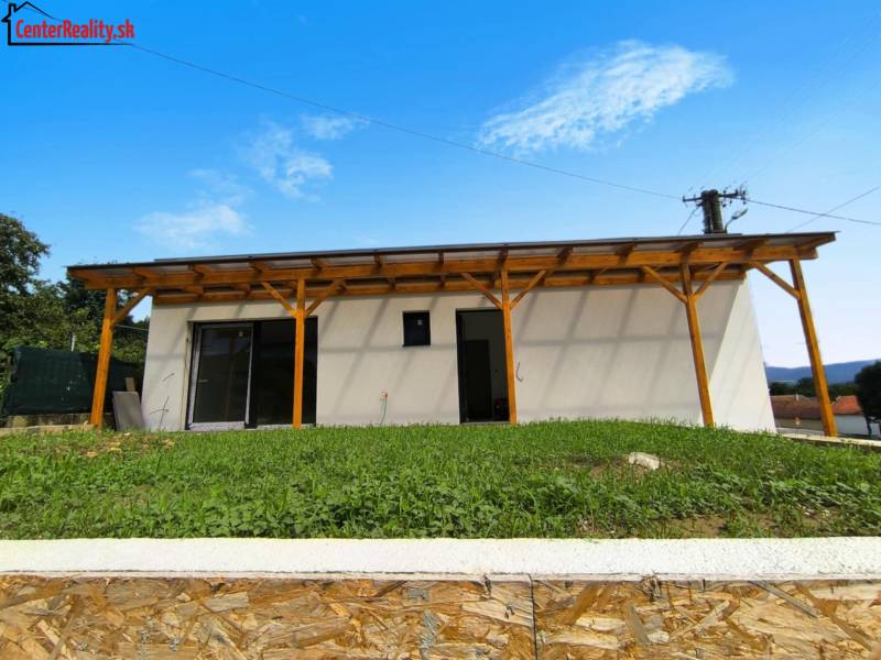 Ein Einfamilienhaus in Malé Kršteňany mit einer Holzpergola und einem Rasen am Hang.