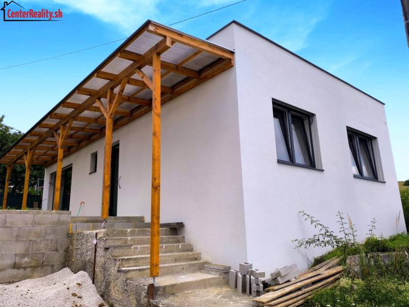 Ein Einfamilienhaus in Malé Kršteňany mit einem Holzvorbau und Betontreppen, blauer Himmel.