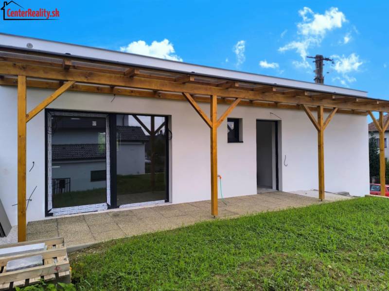 Ein Einfamilienhaus in Malé Kršteňany mit einer Holzpergola und Rasen an einem sonnigen Tag.