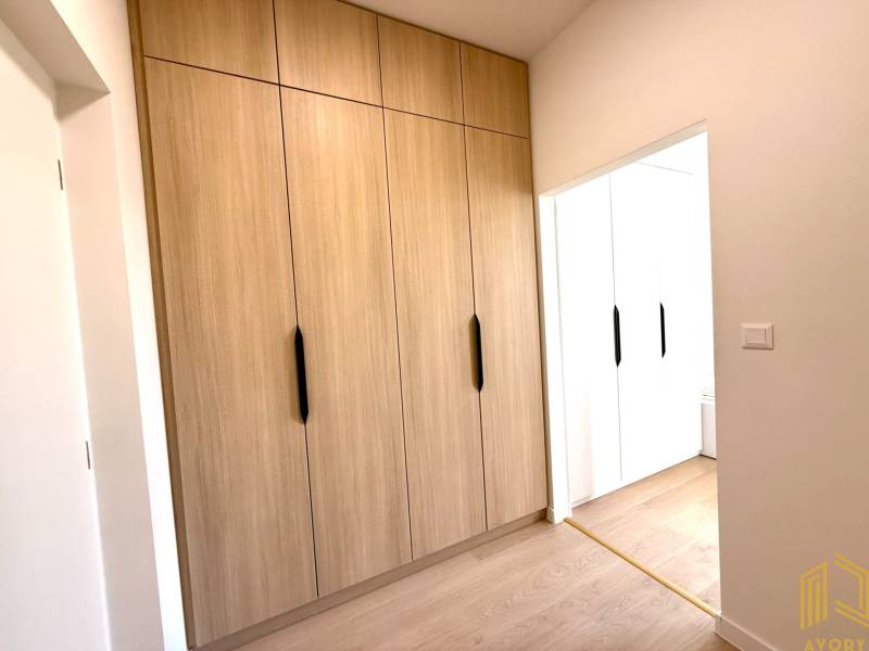 Ein Studio-Apartment mit eingebauten Holzschränken und weißen Wänden wirkt gemütlich.