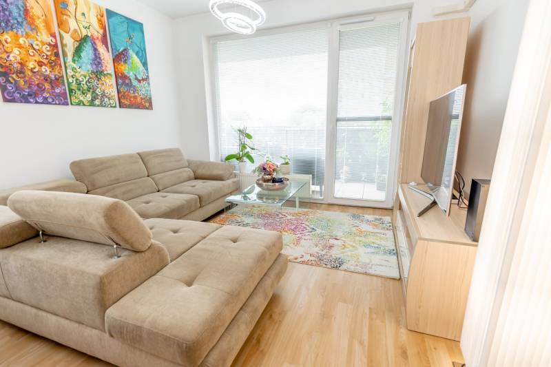 Wohnzimmer mit einem bequemen Sofa, bunten Bildern und großen Fenstern in einer 3-Zimmer-Wohnung.