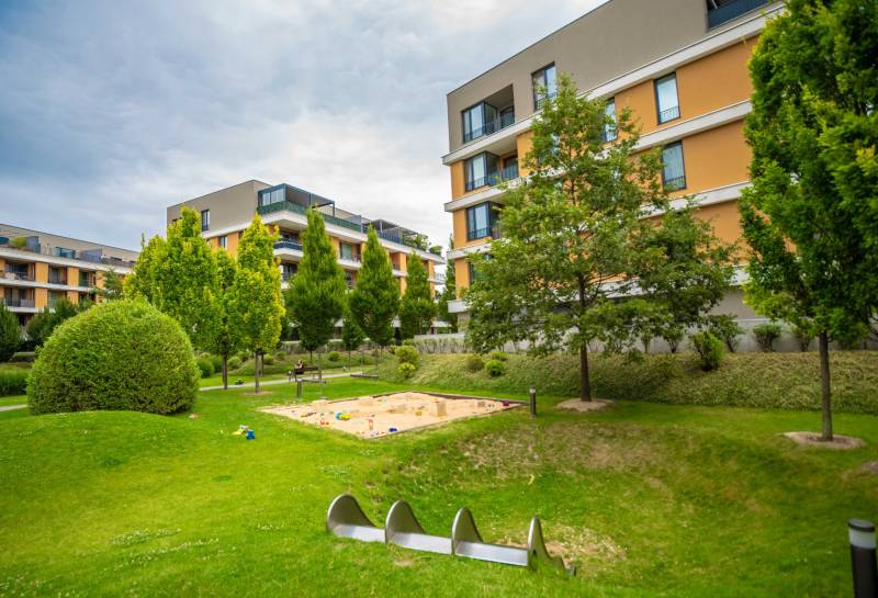 Ein Areal mit mehreren Wohngebäuden, einem Kinderspielplatz und gepflegtem Grün in Bratislava-Ružinov, Bajkalská.
