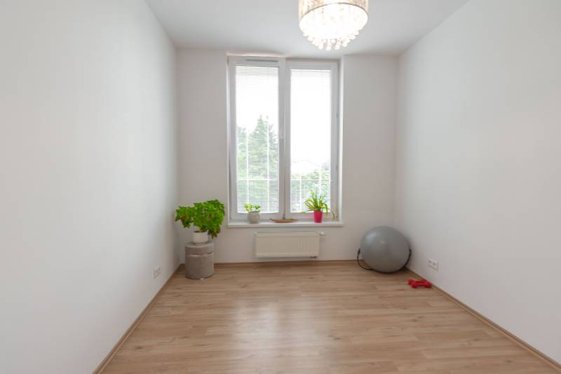 Ein geräumiges Zimmer in einer 3-Zimmer-Wohnung, helle Wände, Blumen und Fitnesszubehör.