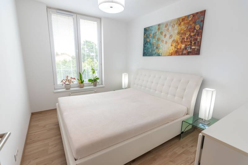 Schlafzimmer in einer 3-Zimmer-Wohnung mit großem Bett, Bild und Blumen auf der Fensterbank.