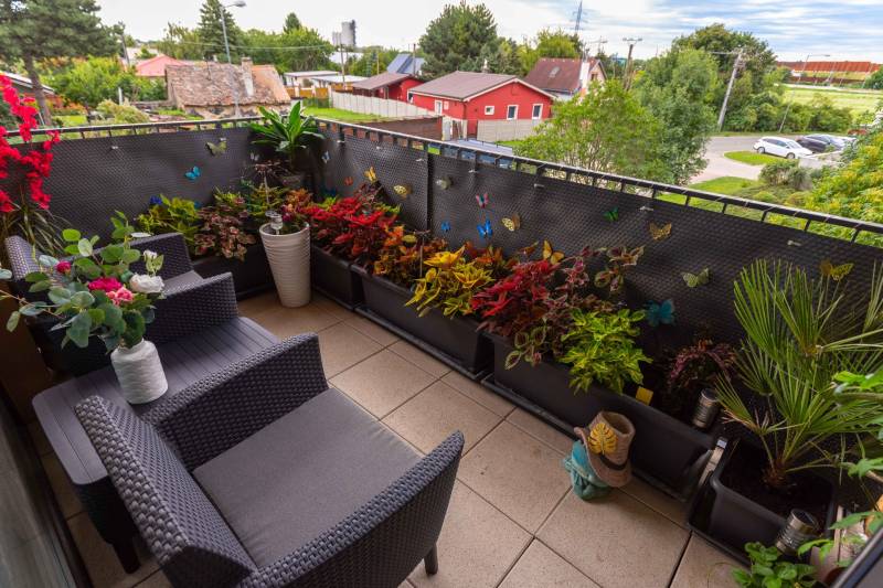 Ein Balkon mit Blumen, Rattanmöbeln und Blick ins Grüne in einer 3-Zimmer-Wohnung.