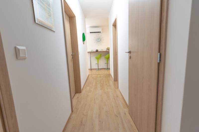 Ein Flur mit Holzboden, der zu grünen Barhockern in einer 3-Zimmer-Wohnung führt.