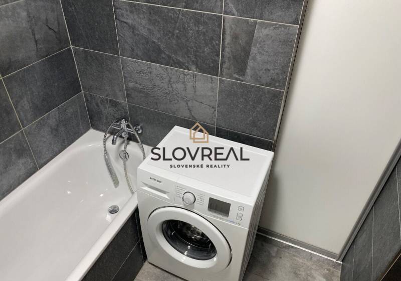 Ein Badezimmer in einer 4-Zimmer-Wohnung mit Badewanne und Waschmaschine in dunkelgrauen Fliesen.